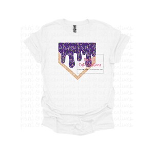 Op de afbeelding: Wit T-shirt met een baseballvormige afbeelding in paars en goud. De afbeelding is een paars, druppelend, gesmolten ontwerp met gouden sprinkels. De tekst "Purple Cut Creations" staat op de afbeelding.