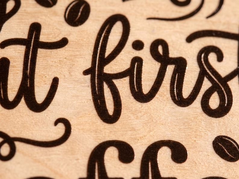 Macro close-up showing sharp, detailed UV printed black lettering on natural birch plywood with a visible wood grain texture.