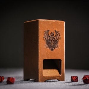 Op de afbeelding: Een houten dobbelsteentoren met een drakenontwerp aan de voorkant. De toren heeft een gleuf om dobbelstenen te rollen en is omringd door rode dobbelstenen.