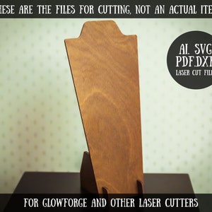 May include: A brown wooden necklace display stand for laser cutting. The stand is designed to hold a necklace upright. The image includes the text "AL. SVG. PDF.DXF. LASER CUT FILES" and "FOR GLOWFORGE AND OTHER LASER CUTTERS".