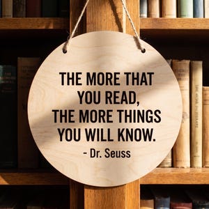 Custom printed wood quote sign hanging in front of a wooden bookshelf featuring a Dr Seuss quote in crisp black lettering.