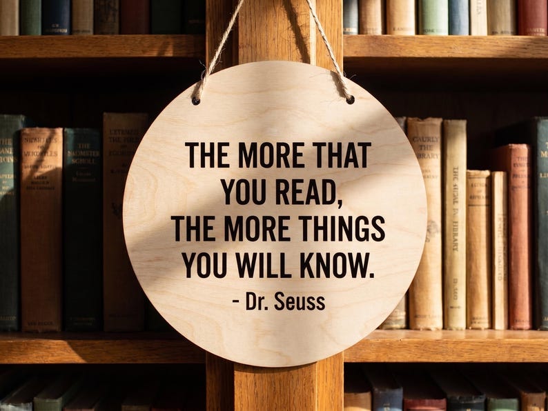 Custom printed wood quote sign hanging in front of a wooden bookshelf featuring a Dr Seuss quote in crisp black lettering.