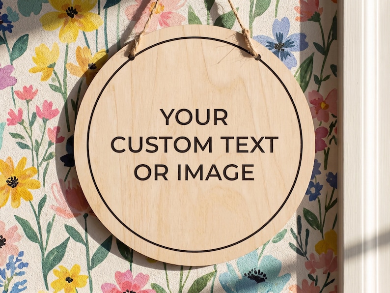 Round wooden hanging sign resting against a colorful floral wallpaper featuring the words your custom text or image printed in the center.
