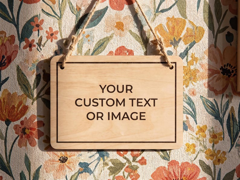Custom wooden hanging sign displaying sample text, suspended by a rustic string against a vintage floral wallpaper background.