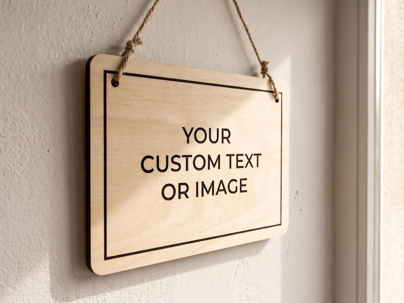 Custom wooden hanging sign with crisp black text on natural birch, illuminated by bright sunlight next to a window.