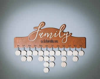May include: Wooden family celebrations calendar with a brown base and white script. The calendar has a scalloped edge and includes 12 months labeled across the top. Below are hanging wooden circles for marking special dates.