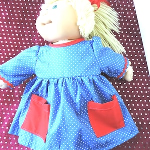 May include: A vintage doll with blonde yarn hair and blue eyes. The doll is dressed in a blue dress with white polka dots, red trim, and two red pockets. A red bow is in the doll's hair. A classic toy.