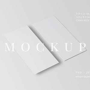 May include: Two white rectangular cards, 9.9 x 21 cm, are slightly angled against a light grey background. The word "MOCKUP" is displayed in a light grey font across the cards. The image also includes the text "PSD + JPG" and "smart object".