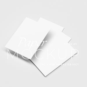 May include: Three white rectangular paper mockups are slightly overlapping, angled against a light gray background. The words "Paper MOCKUP" are written in a delicate, light font across the paper. The text "JPG & PSD SMART OBJECT" is also visible.