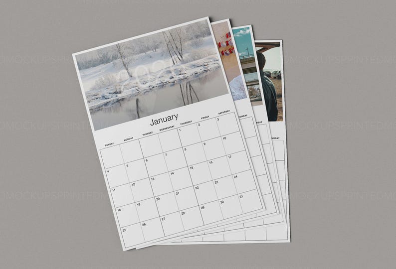 May include: A stack of white paper calendars with a gray background. The top calendar shows the month of January with a winter landscape photo. The calendar grid is black, with the days of the week and dates clearly marked.