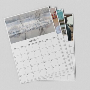 May include: A stack of white 2024 calendars. The top calendar shows a winter landscape with the month of January. The calendar pages have a grid layout with days of the week and dates. The other calendars show different images.