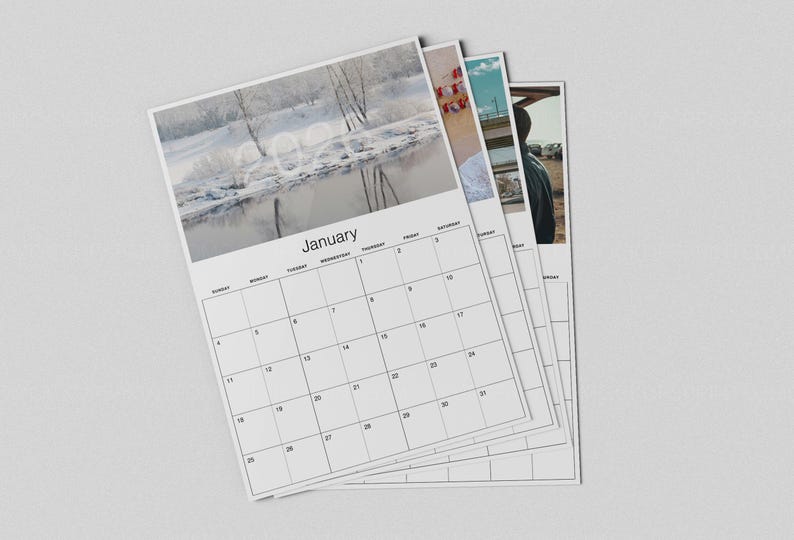 May include: A stack of white 2024 calendars. The top calendar shows a winter landscape with the month of January. The calendar pages have a grid layout with days of the week and dates. The other calendars show different images.