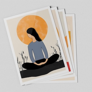 May include: A stack of art prints featuring a minimalist illustration of a person meditating. The artwork depicts a figure in a blue shirt and black pants, with a large orange sun in the background. The prints have a white border.