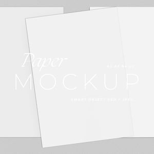 May include: A paper mockup with three white sheets of paper, one angled. The text "Paper MOCKUP" is displayed in a light font. Additional text includes "A2 AT A3" and "SMART OBJECT PSD + JPEG". The background is a light gray.