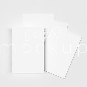 May include: A minimalist mockup featuring several white rectangular cards arranged on a light gray surface. The cards are of varying sizes and orientations, with the words "paper mockup" subtly overlaid in a light font.