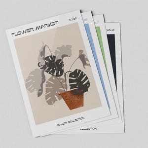 May include: A stack of art prints featuring a botanical illustration of a plant in a terracotta pot. The prints have the text "FLOWER MARKET" and "GALLERY COLLECTION". The prints have a beige, blue, green, and black border.