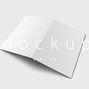 May include: A white, open brochure mockup with the word "mockup" in a light font. The text "PSD + JPG" is below the word "mockup". The brochure is angled, casting a shadow on a light gray background.