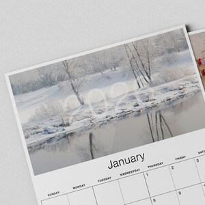 May include: A calendar featuring a winter landscape scene with a river and snow-covered trees. The month of January is displayed at the bottom, with the year 2024 faintly visible in the image. Additional calendar pages are visible.