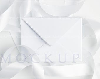Op de afbeelding: Een witte envelop mockup met een witte lint achtergrond. De envelop ligt plat op het oppervlak. De envelop is leeg en klaar voor uw ontwerp.