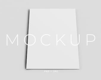 May include: A white mockup of a blank card or brochure on a gray background. The word "MOCKUP" is printed in white text below the card.