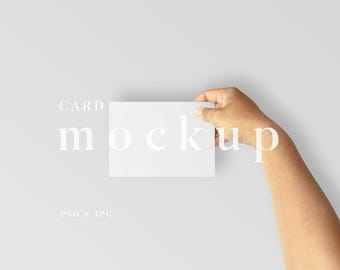 May include: A hand holding a blank white square card against a light gray background. The words "CARD mockup" are printed in a light gray font above the card. Below the card, the text "PSD + JPG" is visible.