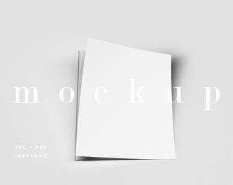 May include: A mockup featuring two white sheets of paper, slightly angled against a light gray background. The word "mockup" is displayed in a serif font. Additional text at the bottom indicates the file types: JPG and PSD, along with "smart object."