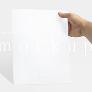 May include: A white A4 paper mockup held by a hand. The paper measures 21.59 x 27.94 cm. The word "mockup" is printed on the paper in a light font. The paper is blank, with a shadow on the left side.