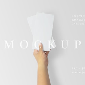 May include: A hand holding two white rectangular cards against a white background. The cards measure 3.9 x 8.3 inches. The word "MOCKUP" is displayed in a light font. The image also includes the text "PSD + JPG smart object".