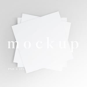 May include: A pile of white square papers arranged in a layered pattern, with the word "mockup" in a light font overlaid on the papers. The text "PSD + JPG" is in the lower left corner. The background is a soft grey.