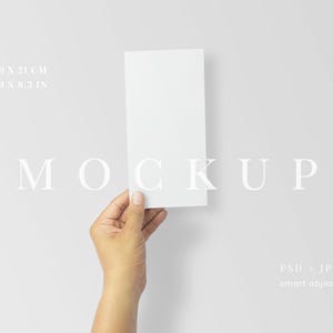 May include: A white rectangular mockup held by a hand against a light gray background. The dimensions are 3.9 x 8.3 inches and 9.0 x 21 cm. The word "MOCKUP" is displayed in a serif font. The image also includes "PSD + JPG" and "smart object".