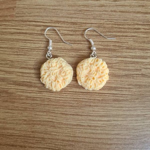 May include: A pair of dangle earrings featuring a light orange, textured, noodle-shaped design.
