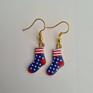May include: A pair of gold dangle earrings featuring red, white, and blue socks with a star pattern.