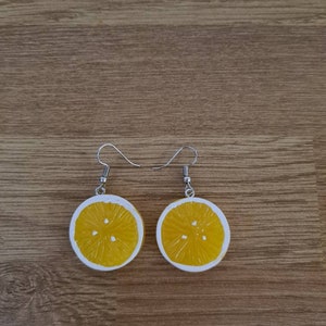 Può includere: Un paio di orecchini a fetta di limone con ganci d'argento. Gli orecchini sono in resina gialla e hanno un contorno bianco.