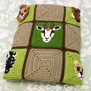 Puede incluir: Una manta de crochet verde y marr&oacute;n con varias aplicaciones de animales, incluyendo un le&oacute;n, una cebra, una ant&iacute;lope y un guepardo. La manta est&aacute; hecha de cuadrados con un borde marr&oacute;n.