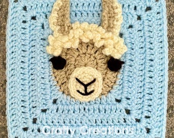 May include: A crocheted square featuring a light blue background with a brown and white llama face in the center. The llama has black eyes and a black nose. The square is surrounded by a white border.