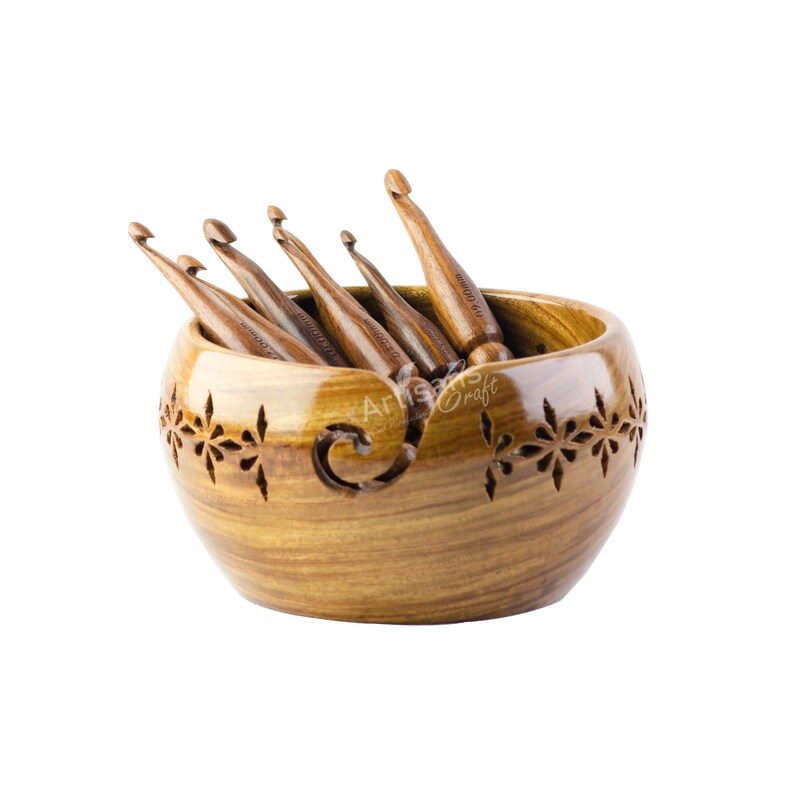 May include: A wooden yarn bowl with intricate carvings and a set of wooden crochet hooks inside. The bowl is brown with a light wood grain and has a floral design carved into the sides. The hooks are also brown and have a smooth finish.