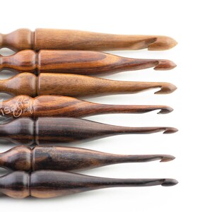 May include: Set of six wooden crochet hooks in various shades of brown. The hooks are arranged in a row, with the largest hook at the top and the smallest hook at the bottom.