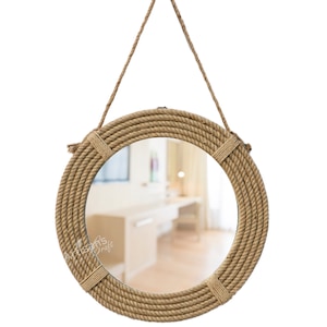 Pode incluir: Um espelho redondo com uma moldura grossa de corda, pendurado em um laço de corda. O espelho reflete uma sala com móveis.