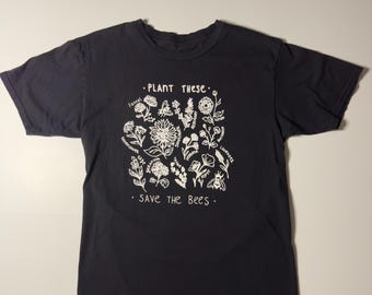 May include: Black t-shirt with a white graphic of flowers and the text "PLANT THESE" and "SAVE THE BEES".