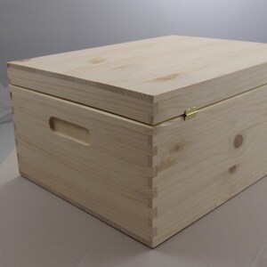 May include: A natural wood storage box with a hinged lid and brass hinges. The box has a handle on the side.