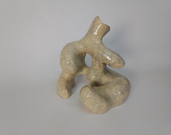 Pode incluir: Uma escultura de cerâmica branca com uma forma orgânica abstrata. A escultura tem uma superfície texturizada e um acabamento liso e brilhante.