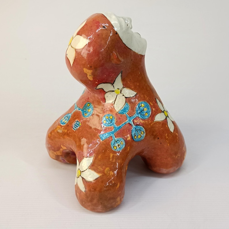 May include: A ceramic sculpture of a stylized figure with a red-brown glaze and white and blue floral designs.
