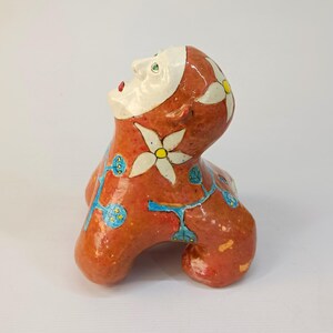 May include: A ceramic sculpture of a stylized human figure with a red, white, and blue floral design. The figure is sitting with its head tilted back and its eyes closed.