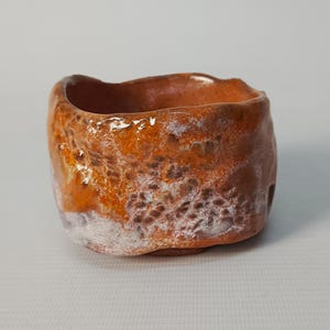 May include: A small, orange and white ceramic planter with a rough, textured surface.