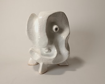 Pode incluir: Escultura de cerâmica branca com uma forma orgânica abstrata. A escultura tem uma superfície lisa e texturizada e apresenta uma série de furos e aberturas.