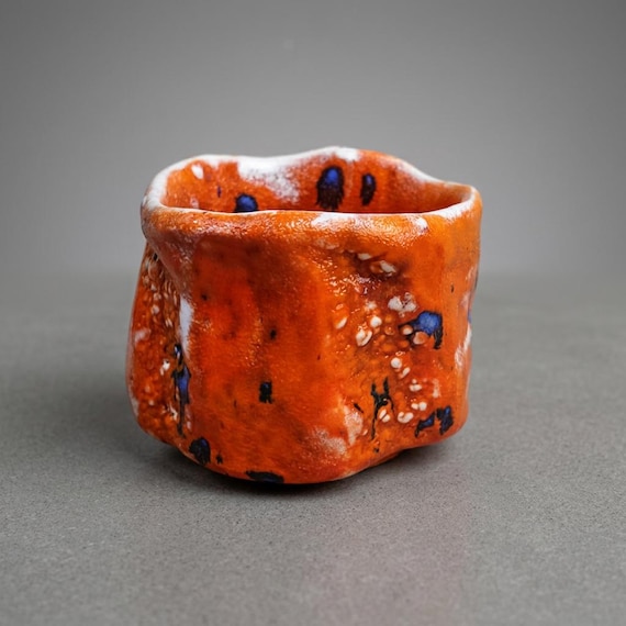 A one-off hand-thrown wabi-sabi bowl with vivid orange glaze and blue flecks — the kind of piece that looks like it belongs in a ceramics gallery, not a big-box store.