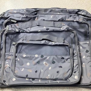 May include: Set of four gray travel packing cubes with a black and white geometric pattern. The cubes are made of a lightweight, water-resistant material and feature a zipper closure.