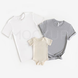 May include: A set of three plain t-shirts in white, grey, and beige. The shirts are laid flat on a white background.