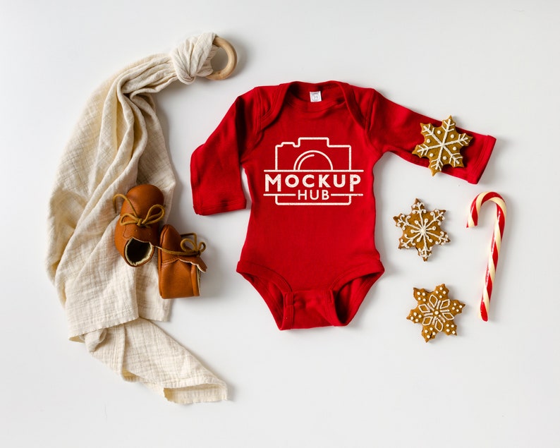 May include: Red baby onesie with long sleeves and a white camera graphic with the text "MOCKUP HUB". The onesie is surrounded by gingerbread cookies and a candy cane.