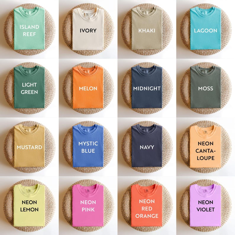 May include: A collection of folded t-shirts in various colors, including green, ivory, khaki, and blue. Each shirt displays a color name in white text, such as "Island Reef" and "Lagoon". The shirts are arranged on round, woven mats.